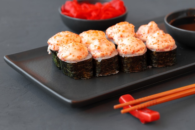 Rollo de sushi al horno servido en placa negra sobre mesa de madera