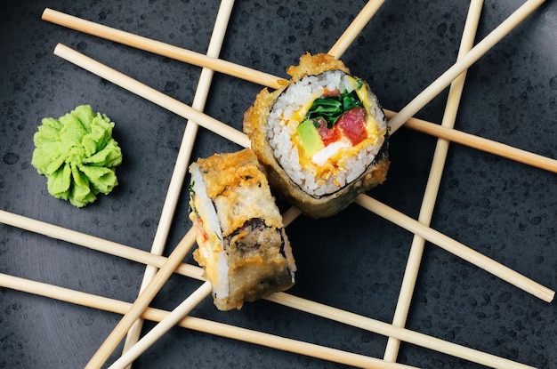 Rollo de sushi de atún casero con aguacate y queso en un empanizado crujiente sobre un plato de piedra oscura.