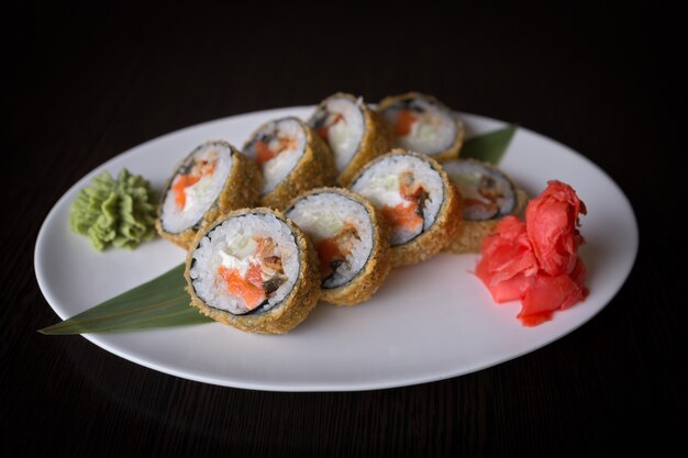 Rollo de sushi caliente con pescado rojo en un plato blanco, sobre una superficie negra