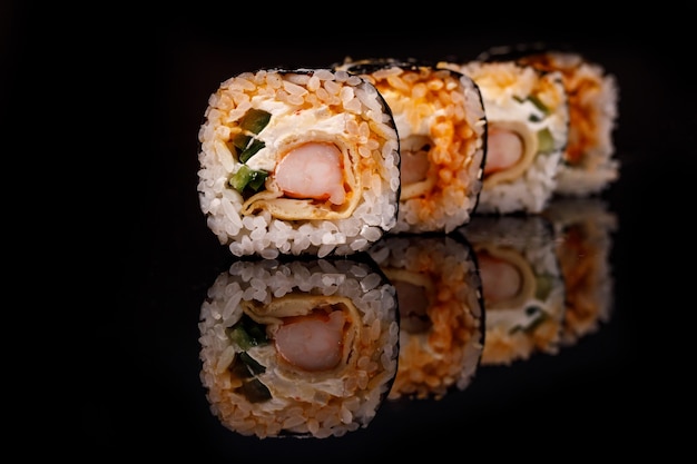 Rollo de sushi con camarones sobre una superficie negra con reflejo.