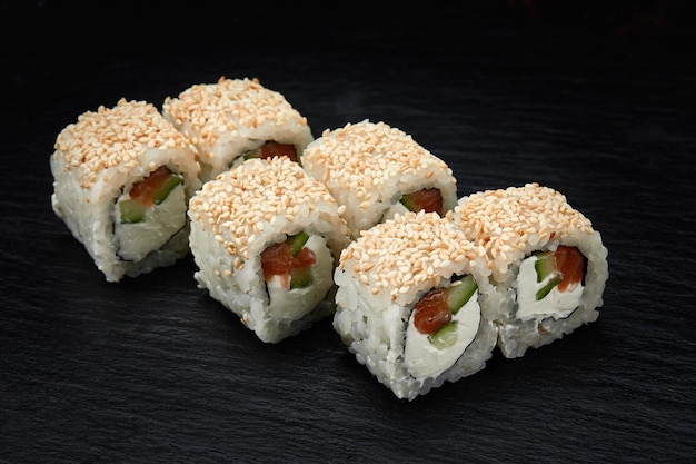 Rollo de sushi fresco delicioso tradicional sobre un fondo negro Rollo de sushi con arroz queso crema aguacate salmón sésamo Menú de sushi de Filadelfia Restaurante de cocina japonesa