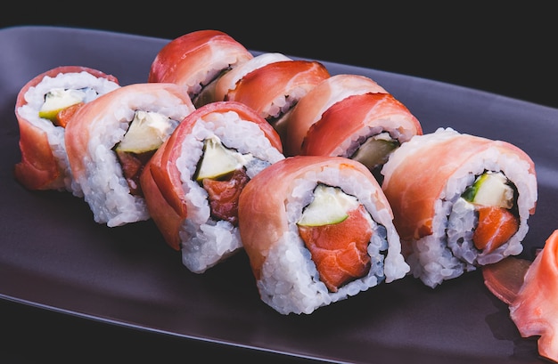 Rollo de sushi japonés con loncha de jamón crudo cortado en placa