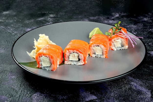 Rollo de sushi japonés con salmón y queso crema. Rollo Filadelfia en una placa gris sobre una superficie negra