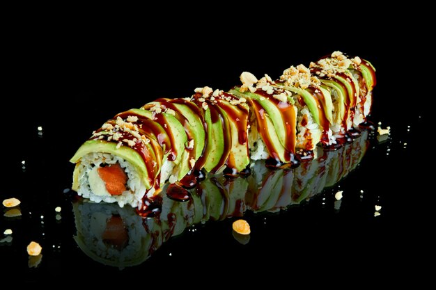 Rollo de sushi japonés tradicional con salmón, semillas de sésamo, aguacate, salsa de unagi y queso crema sobre una superficie negra con reflejo. Foto para el menú