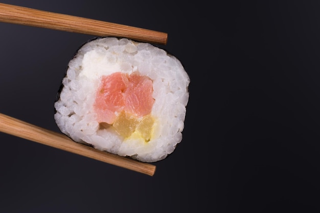 Rollo de sushi con palillos de cerca sobre fondo negro