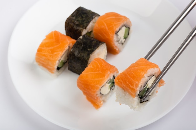 Rollo de sushi en palillos con sushi roll en plato blanco sobre fondo blanco.