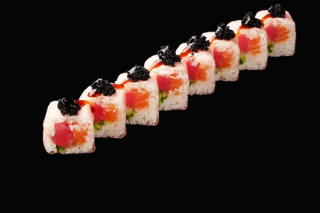 Rollo de sushi con salmón, atún, tobiko negro, caviar, pepino, soja, papel, unagi, salsa, aislado, en, fondo negro