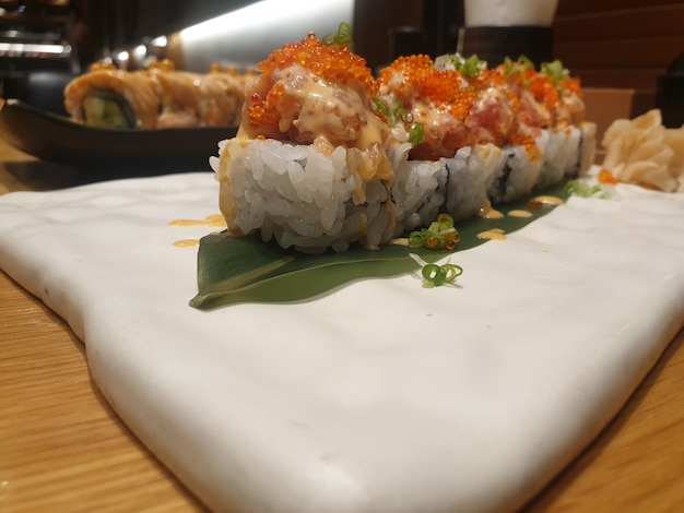 Rollo de sushi con salmón encima dispuesto en un plato blanco Menú de sushi Comida japonesa