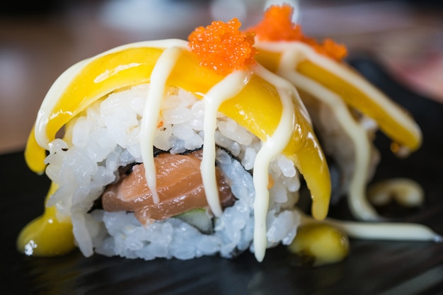 Rollo de sushi de salmón con fruta de mango, estilo de comida japonesa en plato de cerámica negro