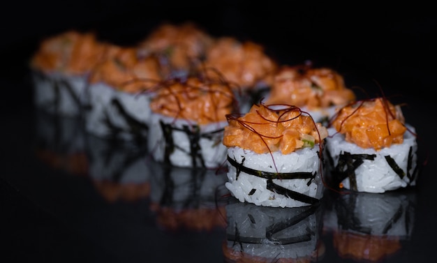 Rollo de sushi con salmón, semillas de sésamo y salsa desde arriba aislado sobre fondo negro con reflexión