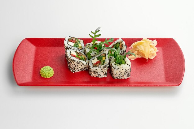 Rollo de sushi de sésamo vegetariano vegetal en un plato rojo sobre un fondo gris