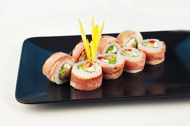 Rollo de sushi con tocino y lubina frita sobre una placa negra