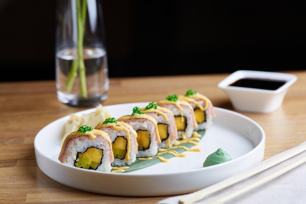 Foto rollo de sushi con tocino en placa de madera con flores y salsa de soja de cerca. concepto de mesa de restaurante