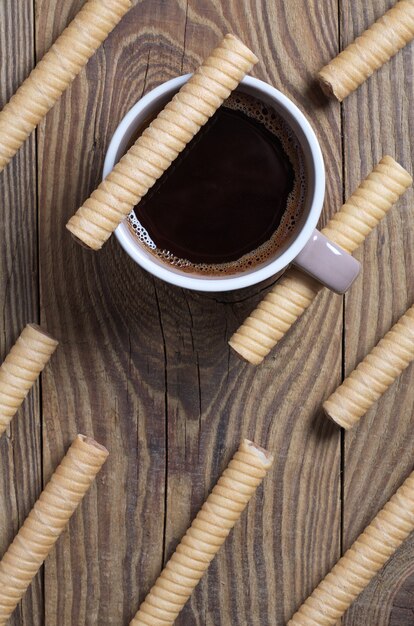 Rollos de barra de obleas de chocolate y una taza de café sobre un fondo de madera, vista superior