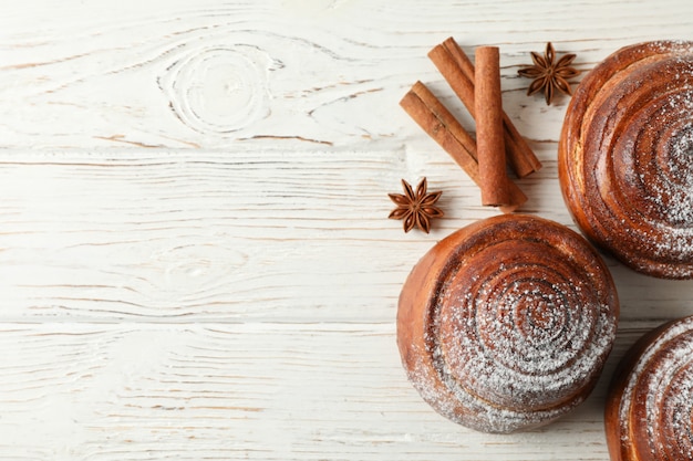 Rollos de canela con azúcar en polvo y palitos de canela en madera blanca