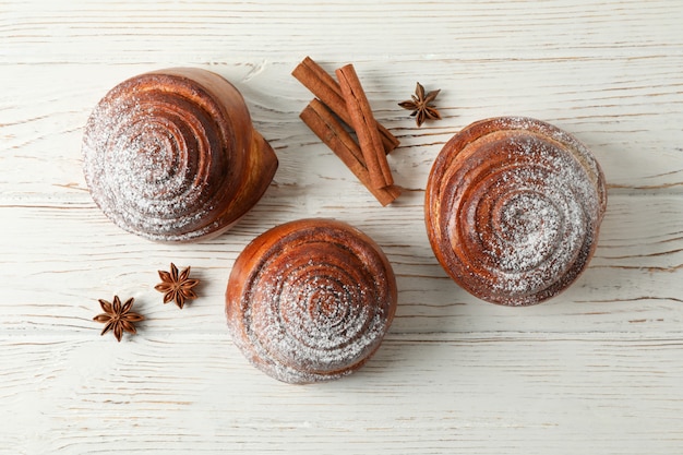 Rollos de canela con azúcar en polvo y palitos de canela en la mesa de madera blanca