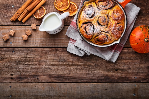 Rollos de canela y canela bollos con calabaza, nueces, caramelo y crema de azúcar helada sobre la mesa de fondo de madera rústica. Vista superior. Dulce repostería casera de Navidad para hornear. Kanelbule - postre sueco.