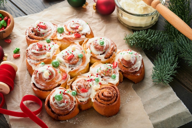 Rollos de canela en forma de árbol de Navidad o bollos de canela con canela y salsa de crema sobre fondo de madera Idea festiva para bollos de postre festivo de invierno tradicional casero para la cena Vista superior