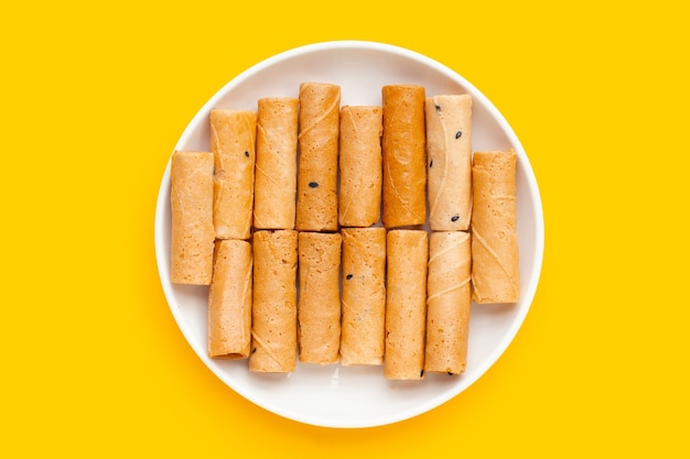 Rollos de coco crujiente tailandés en plato blanco sobre fondo amarillo.