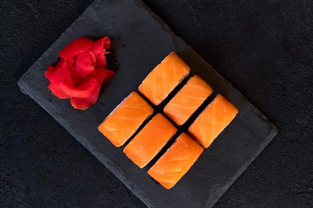Rollos de filadelfia con salmón, pescado, aguacate y queso crema en un plato de piedra sobre fondo oscuro