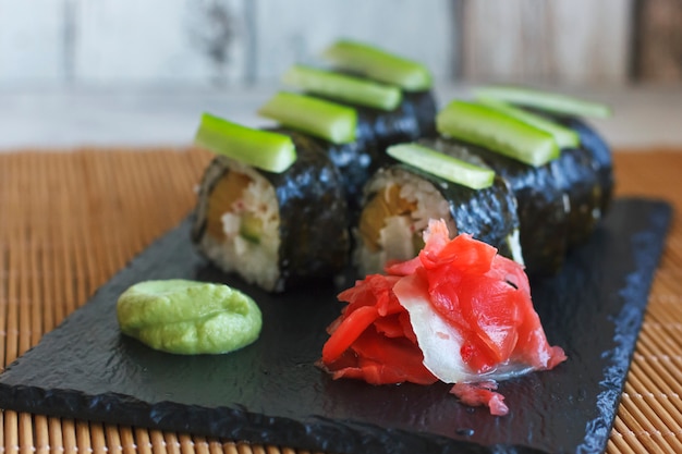 Rollos japoneses con pepino, cangrejos y tortilla en un tablero negro con wasabi y jengibre