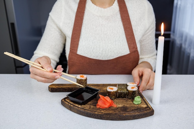 Rollos japoneses con pescado rojo en una caja de cartón abierta Chica comiendo sushi con palillos Decoración de mesa