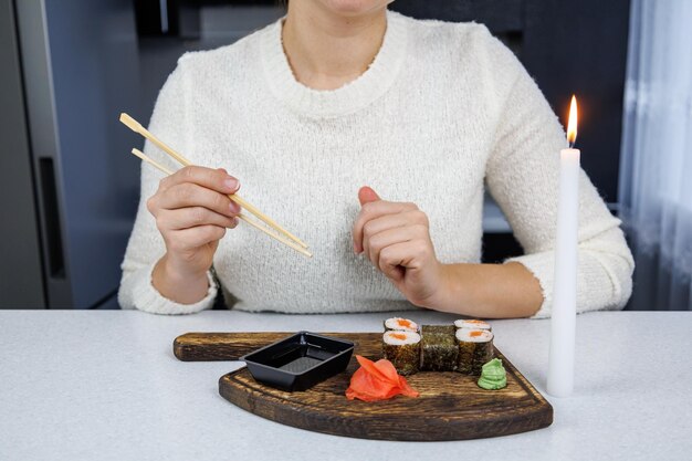 Rollos japoneses con pescado rojo en una caja de cartón abierta Chica comiendo sushi con palillos Decoración de mesa