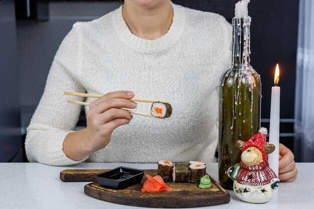 Rollos japoneses con pescado rojo en una caja de cartón abierta Chica comiendo sushi con palillos Decoración de mesa