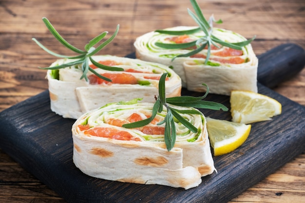 Foto rollos de pan de pita fino y salmón rojo salado con hojas de lechuga sobre una tabla de cortar de madera. copie el espacio.