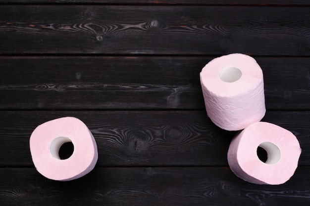 Rollos de papel higiénico rosa pastel en madera negra