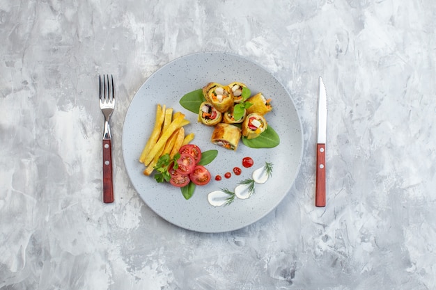 Rollos de paté de verduras de vista superior con tomates y papas fritas dentro de la placa en la superficie blanca