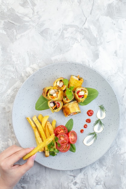 Rollos de paté de verduras de vista superior con tomates y papas fritas dentro de la placa en la superficie blanca