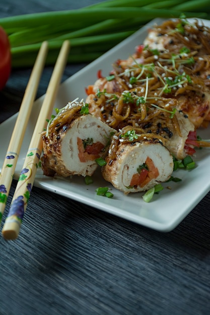 Rollos con pechuga de pollo fresco con verduras, rodajas de zanahoria, pimientos en una tabla de cortar oscura.