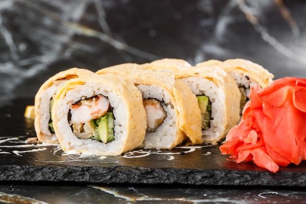 Rollos de sushi con aguacate, anguila, pepino y queso crema dentro de pizarra negra aislada sobre fondo de mármol negro. California rolls cubiertos de tortilla Menú de sushi. Foto horizontal
