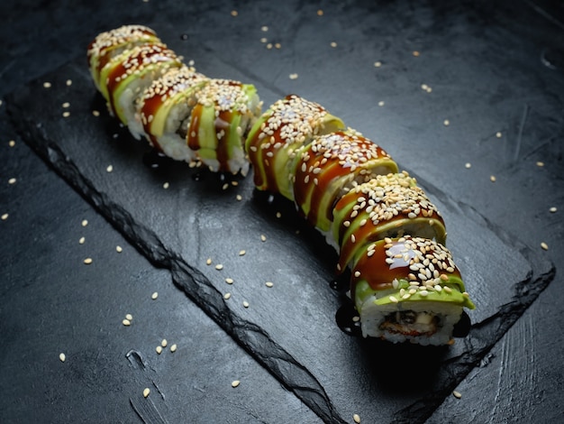 Rollos de sushi de aguacate dragón verde sobre fondo oscuro. Arte de fotografía de comida creativa. Comida de la cocina japonesa