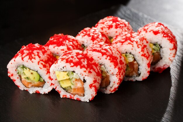 Rollos de sushi con aguacate, pepino y salmón en el interior en negro