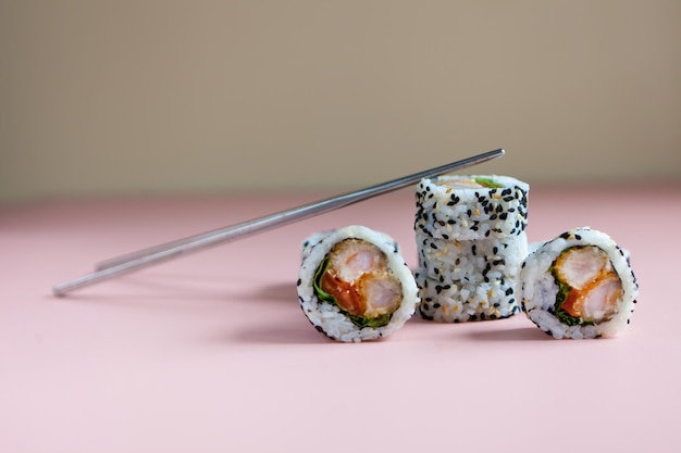 Rollos de sushi con camarones sobre fondo rosa palitos de sushi reutilizables Alimentos Fotovariedades de sushis