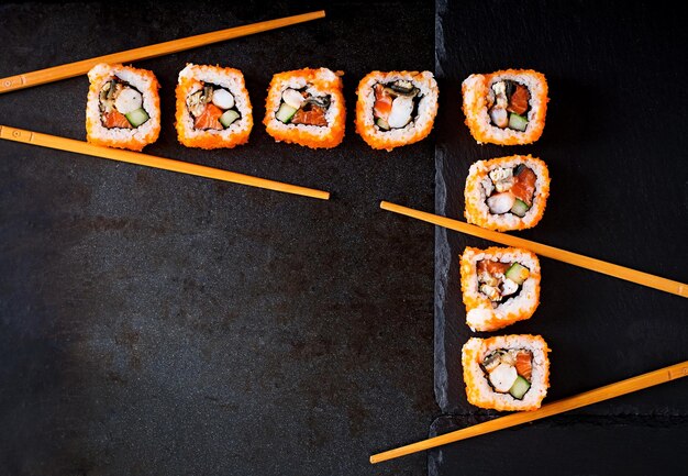 Rollos de sushi de comida tradicional japonesa y palillos para sushi en un fondo oscuro Vista superior