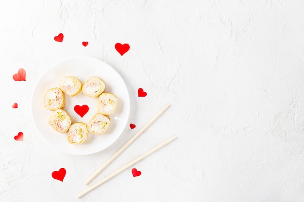 Rollos de sushi para el día de San Valentín con corazones rojos en un plato blanco.