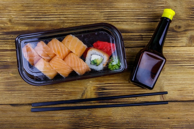 Rollos de sushi Filadelfia en caja de plástico sobre mesa de madera Vista superior