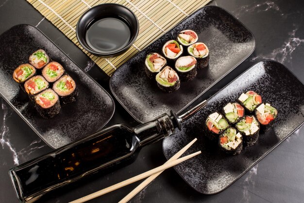 Rollos de sushi frescos y sabrosos con palitos y salsa sobre fondo negro