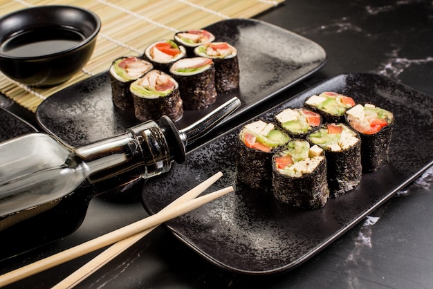 Rollos de sushi frescos y sabrosos con palitos y salsa sobre fondo negro