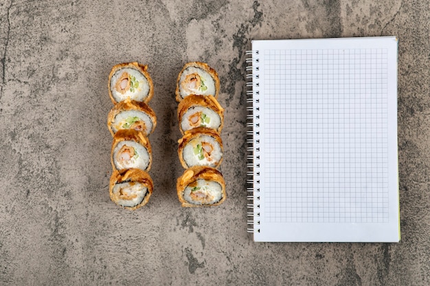 Rollos de sushi frito caliente con salmón y cuaderno vacío en la mesa de piedra.