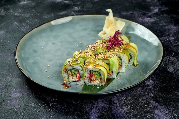 Rollos de sushi japonés con anguila y aguacate en una placa azul sobre una superficie negra. Rollo dragón verde