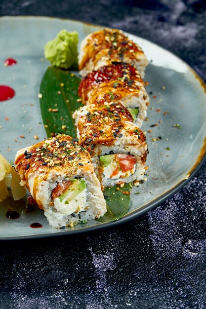 Rollos de sushi japonés con anguila, salmón, aguacate y queso crema en una placa azul