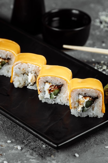 Rollos de sushi japonés fresco tradicional sobre una piedra negra Teka Kaji. Ingredientes del rollo: queso cheder, queso philadelphia, pepino, chips de atún, nori, arroz