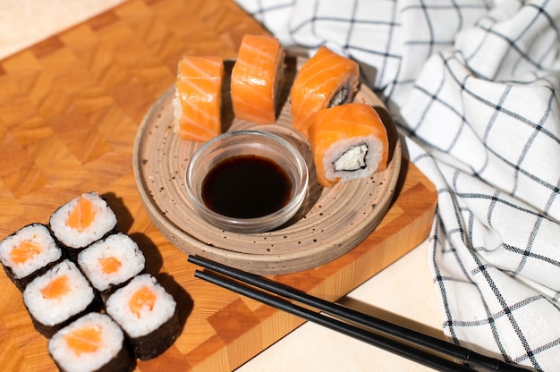 Rollos de sushi japonés servido en plato sobre fondo de madera. Sushi rolls Philadelphia, maki, palillos y salsa de soja