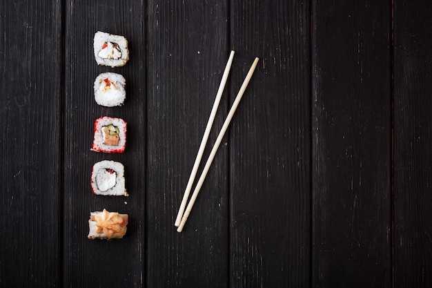 Rollos de sushi japoneses y palillos sobre una tabla de madera negra Vista desde arriba