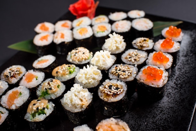 Rollos de sushi japoneses servidos en plato negro sobre fondo oscuro