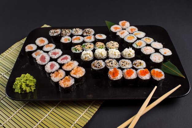 Rollos de sushi japoneses servidos en plato negro sobre fondo oscuro